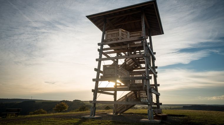 Houten uitkijktoren bij zonsondergang met weids uitzicht over het landschap.