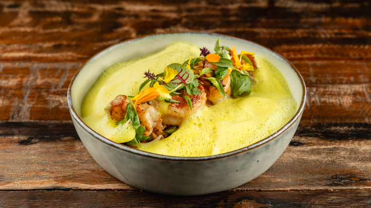 Un plat élégant dans un bol, garni d'une mousse verte et de légumes colorés. La composition semble fraîche et attrayante.
