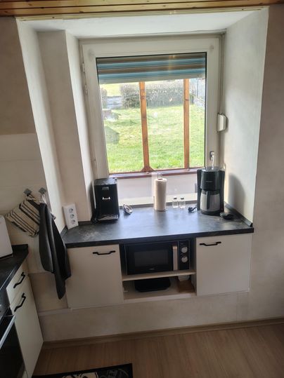 A modern kitchen with a window that overlooks the green meadow. On the countertop are a coffee machine, a kettle, and a microwave.