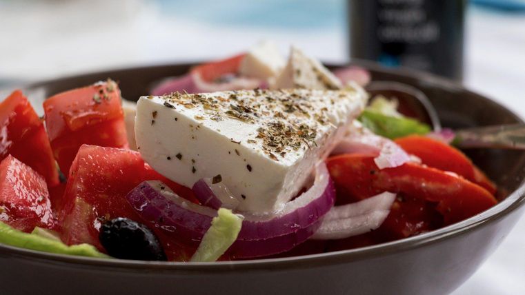 <p>Symbolbild- eine dunkle Salatschüssel gefüllt mit roter Paprika, roten Zwiebeln, grünem Salat und Oliven.Auf dem Salat liegt ein dreieckiges Stück weißer Käse.</p>