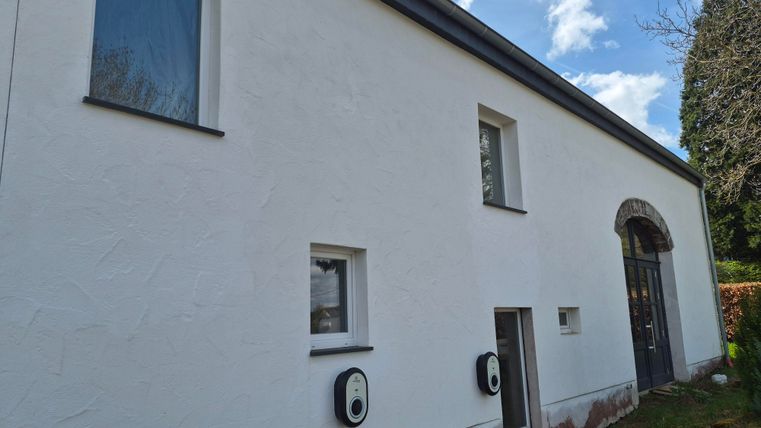 Een modern, wit huis met vensters en een deur in een stijlvol ontwerp. Aan de muur zijn twee oplaadpunten geïnstalleerd.