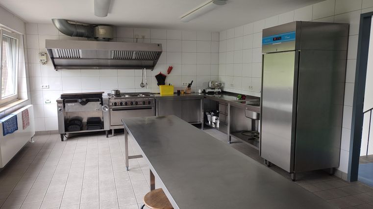 Une cuisine moderne et bien équipée avec des appareils en acier inoxydable et une grande table. Il y a un réfrigérateur et divers ustensiles de cuisine.