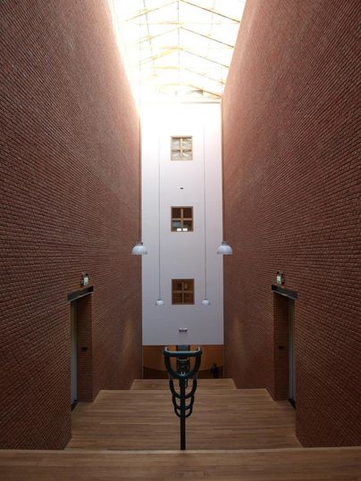 Ein moderner Innenraum mit rotem Mauerwerk und Holzfußboden. Licht strömt durch ein Glasdach und beleuchtet den Raum.