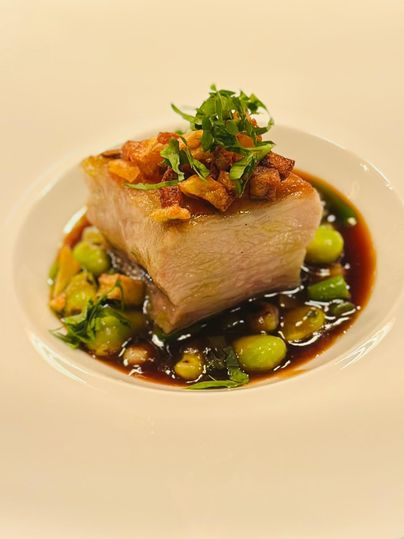 Een kunstzinnig gepresenteerd gerecht met een sappig stuk vlees, gegarneerd met krokante uien en verse kruiden. Omringd door een pittige saus en groene bonen.