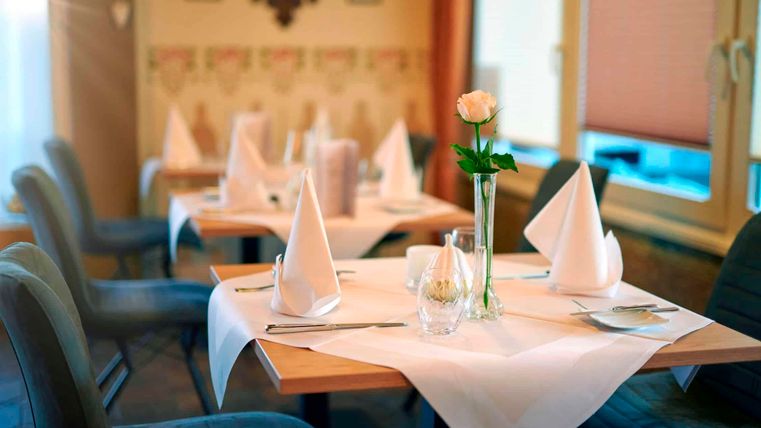 Een elegante tafel in een restaurant met witte tafelkleden en gevouwen servetten. Een roos in een vaas siert de tafelschikking.