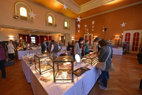 A bustling market in a large room with various booths. People are looking at the products on display and interacting with one another.