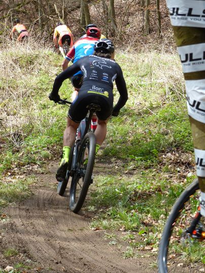 Een mountainbiker rijdt over een bospad. Op de achtergrond zijn meer fietsers te zien die hetzelfde pad gebruiken.
