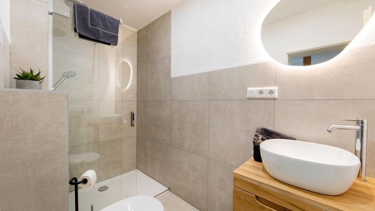 Ein modernes Badezimmer mit Dusche und einem eleganten Waschbecken. Helle Fliesen und ein runder Spiegel sorgen für ein angenehmes Ambiente.