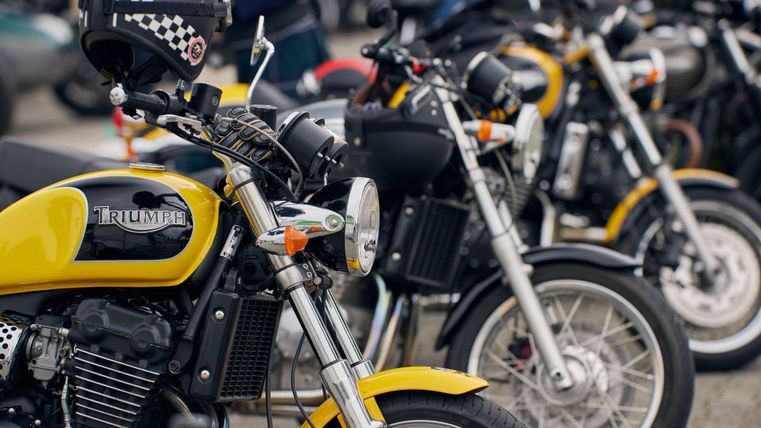 Een reeks motorfietsen in verschillende kleuren staat naast elkaar. De voorste motorfiets is geel en heeft een klassiek ontwerp.