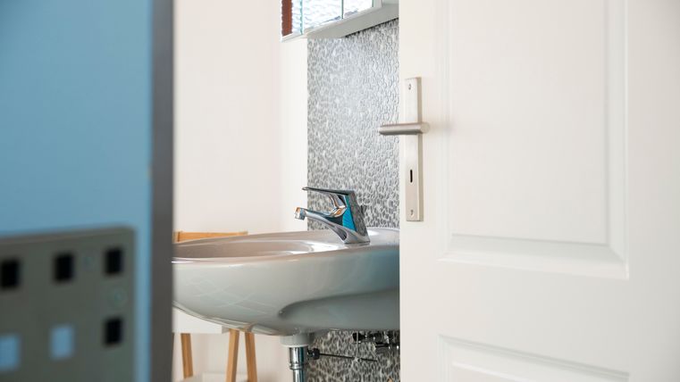 Een moderne badkamer met een elegant wastafel en een heldere kraan. De open deur toont een minimalistische ruimte met een stijlvolle wandafwerking.