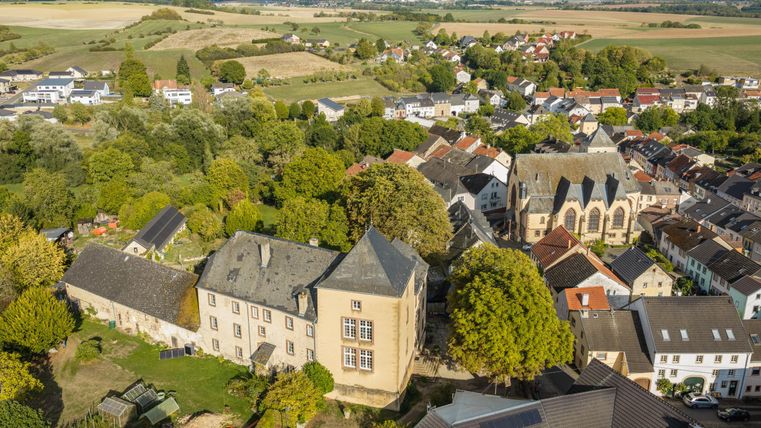 Een schilderachtig stadslandschap met oude gebouwen en een groene omgeving. Op de achtergrond zijn zachte heuvels en een heldere lucht te zien.