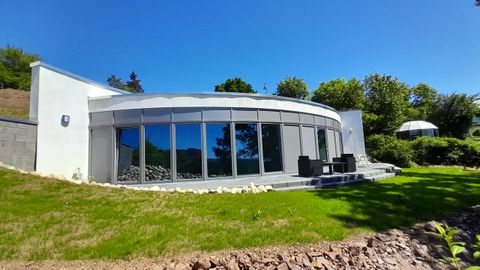 Een modern, rond huis met grote ramen en een mooie tuin. De omgeving is groen en baadt in het licht.