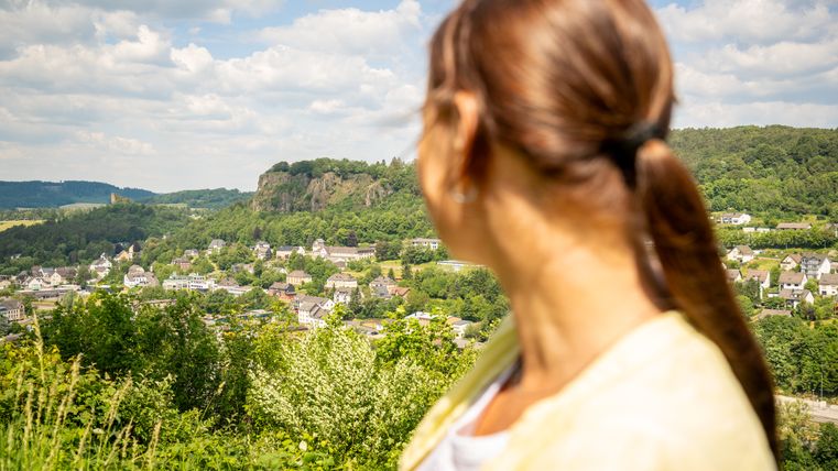 Une femme regarde un paysage verdoyant avec une ville en arrière-plan.