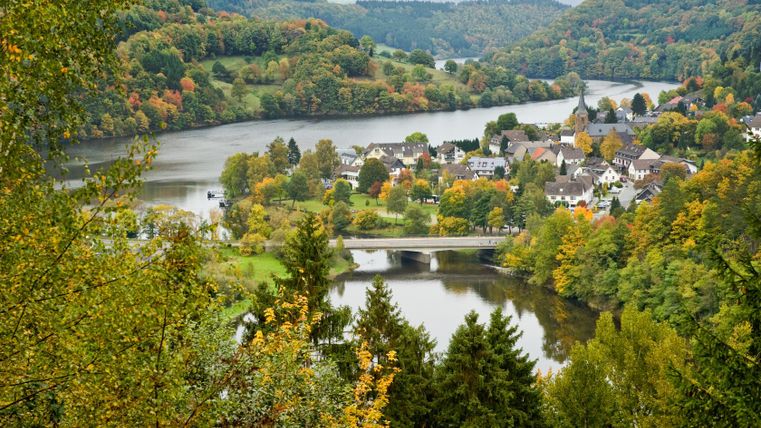 Uitzicht op Einruhr met rivier en brug, omringd door herfstbomen.