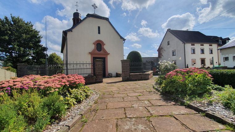 Dorpskerk in Sefferweich met bloemperken en geplaveid pad.