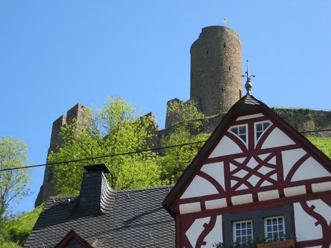 Un vieux château se dresse sur une colline, entouré de verdure. Au premier plan, une maison à colombages traditionnelle est visible.