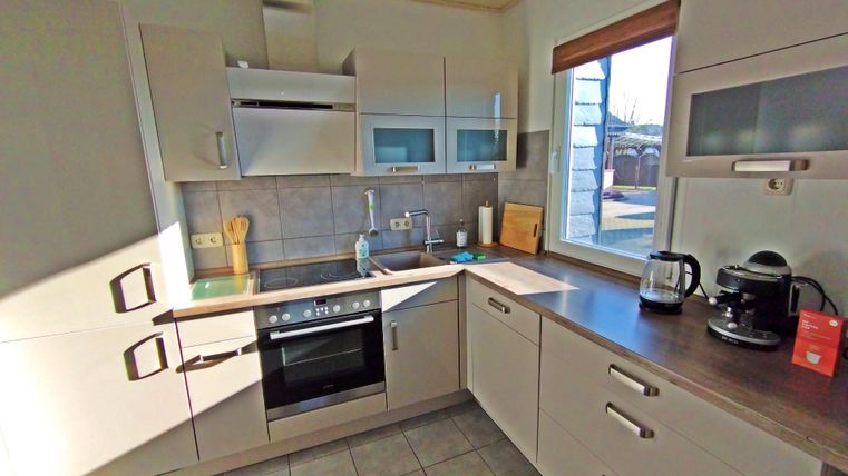 Une cuisine moderne avec des armoires claires et une grande fenêtre. La pièce est bien équipée avec une cuisinière, une cafetière et d'autres ustensiles de cuisine.