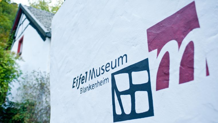 Een bord van het Eifel Museum in Blankenheim, dat de gevel van een gebouw siert. Het toont de naam van het museum en een modern logo.