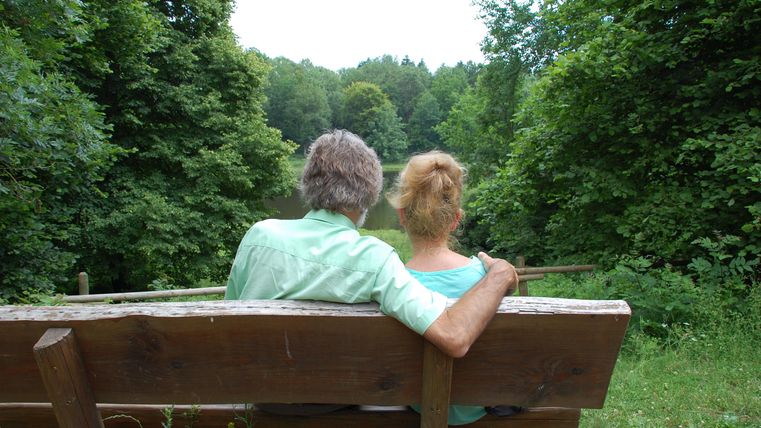 Een ouder paar zit op een bank in het groen.
Ze genieten van de rust en het uitzicht op de natuur.