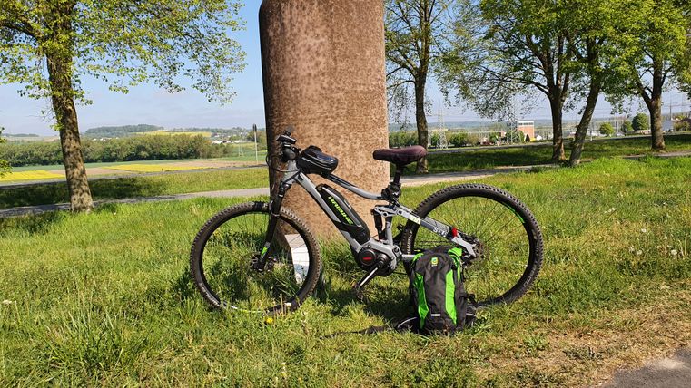 Fiets leunend tegen een stenen pilaar in een weiland, omringd door bomen en platteland.