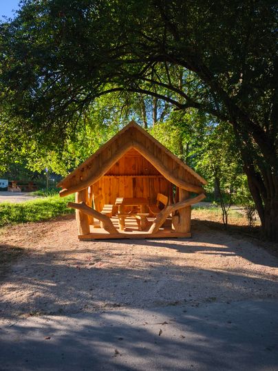 Une maison en bois confortable se trouve sous les arbres. Le ciel dégagé et l'environnement verdoyant créent une atmosphère accueillante.