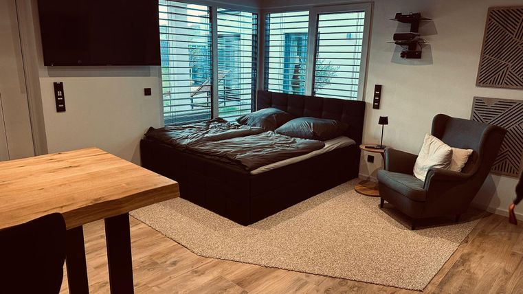 Une chambre moderne avec un lit double et de grandes fenêtres. L'espace est lumineux et accueillant, avec un sol en bois et un tapis.