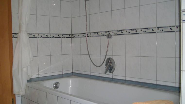 Een eenvoudige badkamer met een bad en een douche. De muren zijn betegeld en er ligt een handdoek op de rand van het bad.