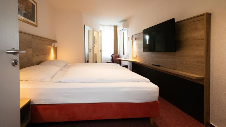 A modern hotel room with a large double bed and a flat-screen TV. The room is brightly and cheerfully decorated.