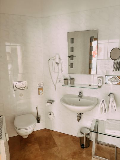 Une salle de bains moderne avec des murs blancs et un miroir. Il y a des lavabos, des toilettes et des serviettes bien visibles.
