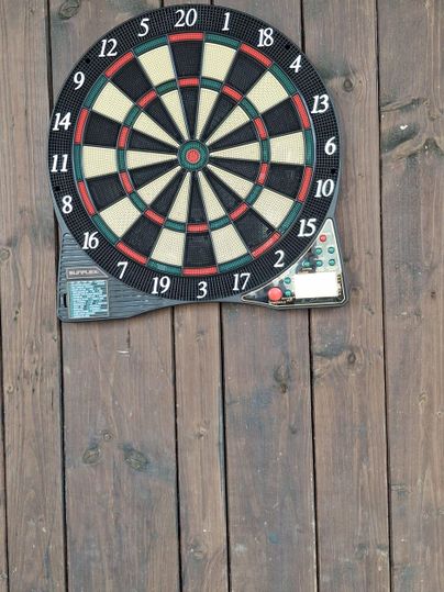 Une cible de fléchettes sur un mur en bois. La cible a les chiffres et les couleurs typiques.