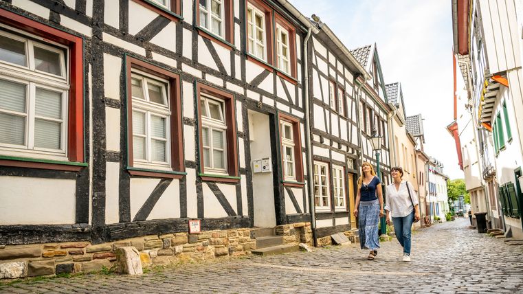 Two women walk along a cobbled street in Bad Münstereifel past traditional half-timbered houses.