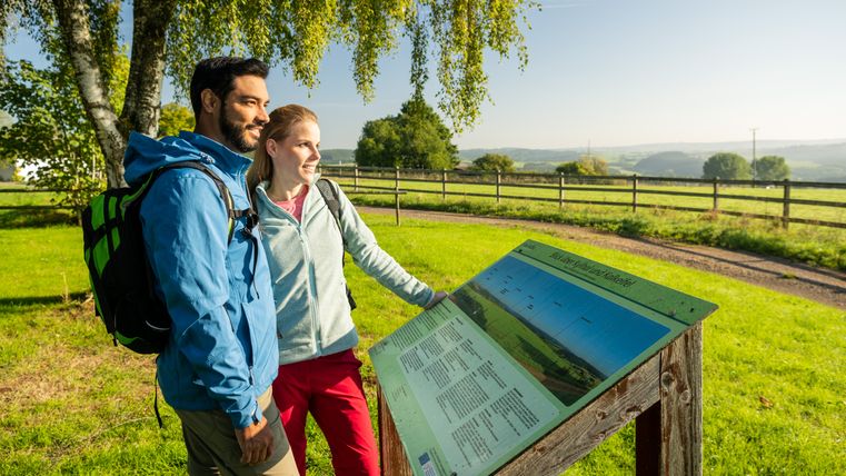 Deux personnes regardent un panneau d'information dans un paysage verdoyant.