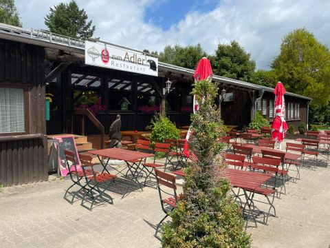 Ein Restaurant mit Außenbereich und Holzmöbeln. Rote Sonnenschirme stehen auf dem Platz unter einem klaren Himmel.