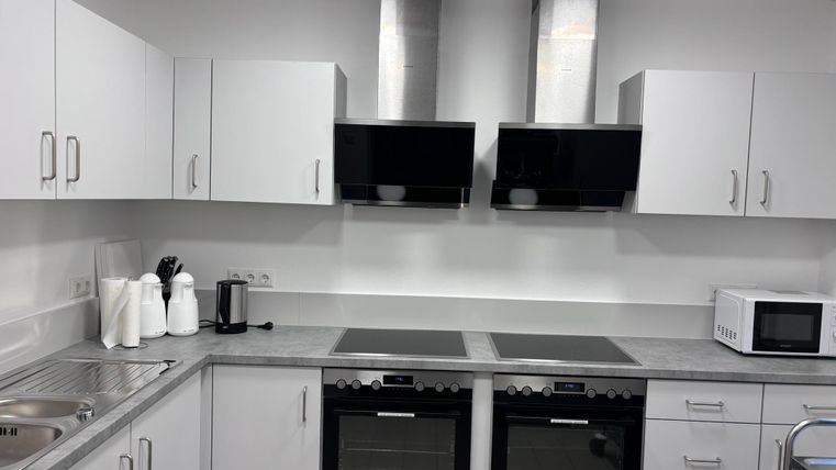 Une cuisine moderne avec des armoires blanches et un plan de travail gris. Elle est dotée de deux plaques de cuisson, de deux fours et d'un four à micro-ondes.