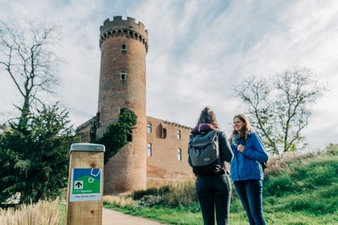Two people stand in front of a historic tower in Zülpich, with a signpost for the Eifelspur in the foreground.