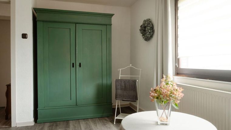 Une pièce confortable avec une armoire verte et une petite table. Sur la table se trouve un vase avec des fleurs, et une chaise confortable est dans le coin.