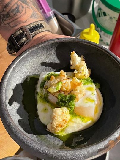 Een heerlijk gerecht met een gepocheerd ei, gegarneerd met krokante stukjes en een groene saus. Het eten wordt gepresenteerd in een donkere kom.