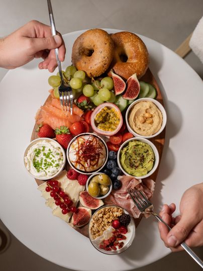 A rich breakfast board with salmon, various fruits, bagels, and dips. The colors and textures invite enjoyment.