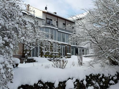 Ein schneebedecktes Haus umgeben von winterlichen Bäumen. Die Fenster spiegeln die Ruhe der verschneiten Landschaft wider.