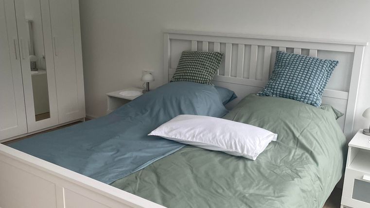 Ein gemütliches Schlafzimmer mit einem großen Bett und zwei verschiedenen Bettdecken. Der Boden ist aus Holz und es gibt einen Kleiderschrank sowie Nachttische.