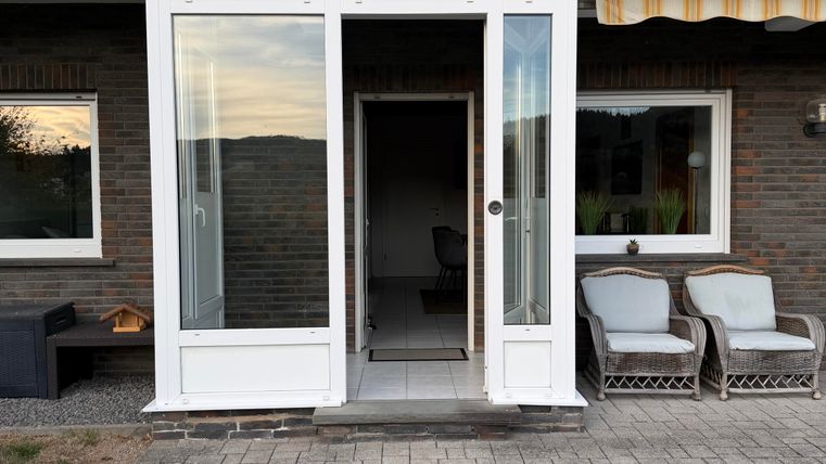 An inviting entrance area with large windows and a modern door. Comfortable chairs are placed on the porch, and the space feels bright and friendly.