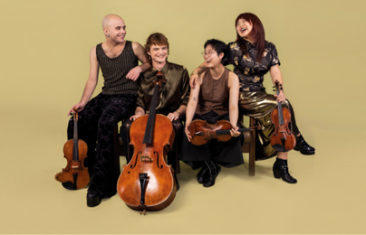 Eine Musikerin sitzt auf einer Bank und hält eine Gitarre. Sie trägt ein elegantes Outfit und schaut in die Kamera.