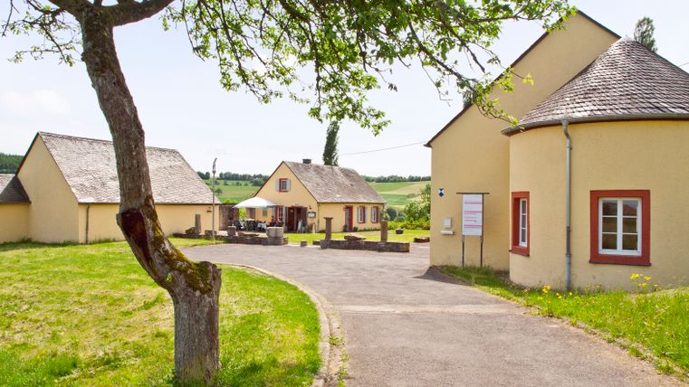 Romeinse villa Ortrang in Fliessem met gele gebouwen en groene boom op de voorgrond.
