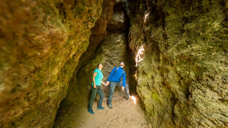 Two people in a narrow, rocky cave looking upwards.
