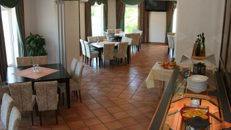An elegant dining room with tables and chairs. On one side, there is a buffet with various dishes.
