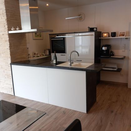 Een moderne keuken met een centraal eiland en stijlvolle, minimalistische design. De ruimte is helder en goed uitgerust met kookapparatuur.