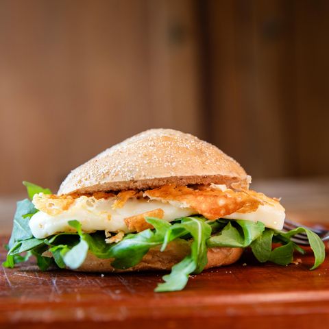 Ein frischer Hamburger mit knusprigem Fischfilet und grünen Blättern auf einem rustikalen Holzbrett. Der Brötchen ist voll und appetitlich gestaltet.