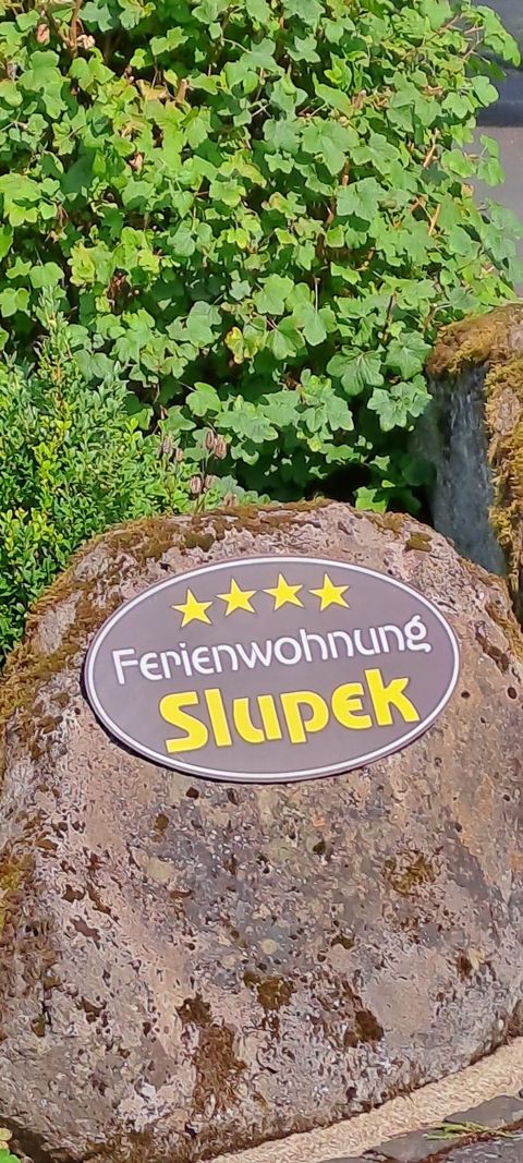 Une enseigne qui indique le gîte « Slupek » avec quatre étoiles. Elle se trouve sur une grande pierre ronde devant un arrière-plan vert.