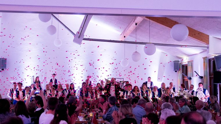 A festive event with many guests who are applauding. On stage stands a group of musicians, while colorful confetti flies through the air.