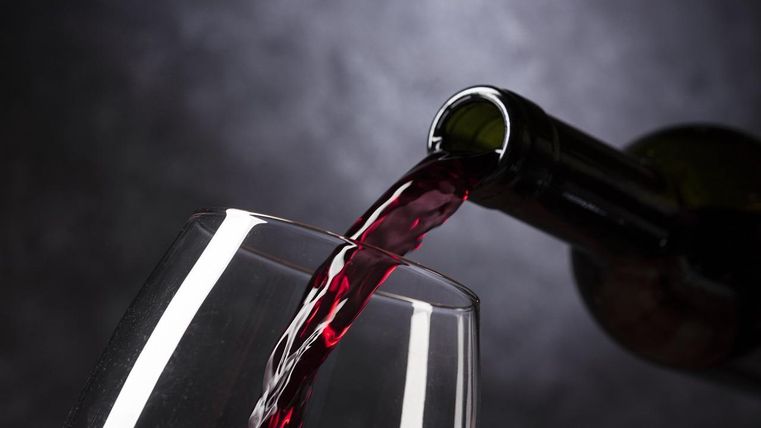 A red wine is being poured from a bottle into a wine glass. The scene is elegantly and darkly set.